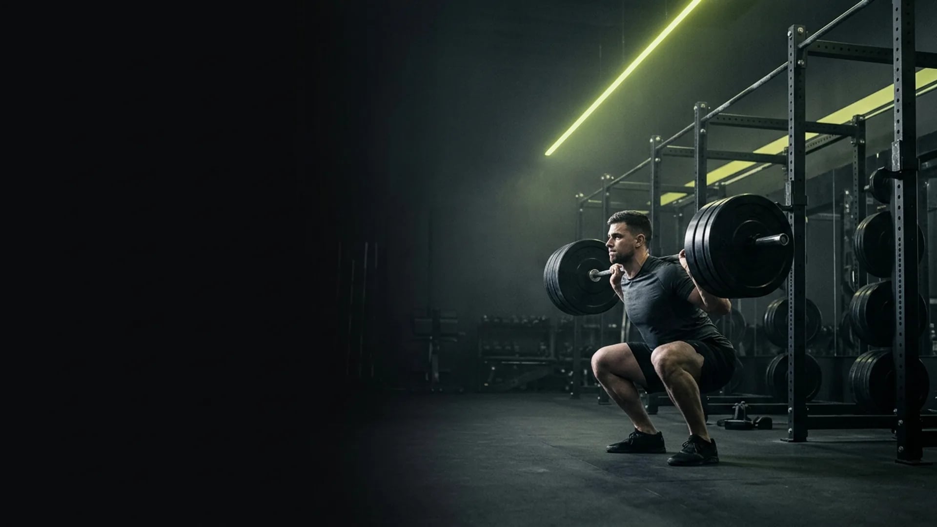 Athlète en plein squat sous une barre olympique chargée, dans la salle de sport et de musculation Cadence à Lyon Confluence, traversée par un trait de lumière vert acide.